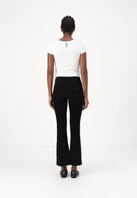 Balts īsām piedurknēm T-krekls ar melnu mieru rokas grafiku uz aizmugures, kombinēts ar pieguļošām melnām izplešamajām džinsām un melnu apavu pāri.