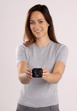 Schwarze Ledertragetasche mit strukturiertem Finish, ausgestattet mit einem Druckverschluss und eingeprägtem Logo, von Händen gehalten, vor einem hellen Hintergrund.