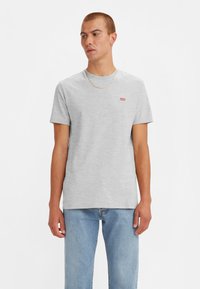 Tricou din bumbac gri cu guler rotund, având un mic logo roșu Levi's pe piept, asortat cu blugi din denim deschis.