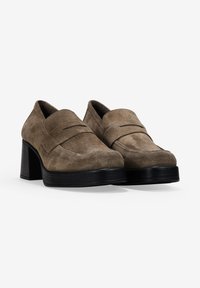 Zapatos de tacón de ante marrón con punta redondeada y un panel delantero elevado. Los tacones son negros y gruesos, proporcionando un soporte estable.
