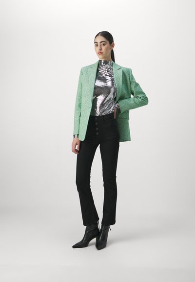 Blazer en velours vert sur un top en sequins argentés, associé à un jean noir taille haute et des bottines noires à bout pointu.