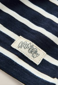 Baumwollstoff mit marineblauen und cremefarbenen Streifen. Ein sichtbares gewebtes Etikett trägt die Aufschrift "RAINBOW" und ist mit einer strukturierten Oberfläche am Rand angenäht.