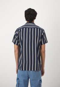 Polo majica s kratkimi rokavi, ki ima vertikalne mornarsko modre in bele črte, izdelana iz mehke tkanine s sproščenim krojem in koničastim ovratnikom.
