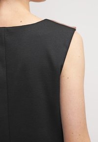 Robe noire sans manches avec un design épuré, un tissu texturé et un accent clair contrastant au niveau de la couture de l'épaule.