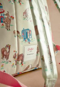 Rucsac cu un material crem, decorat cu modele colorate de cai și flori. Include o zonă de etichetă cu marca "Cath Kids" și bretele roz.