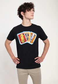 Sort bomulds-T-shirt med en legesyg grafik af dyr på spillekort i gul, beige og hvid, med blå og orange accenter.