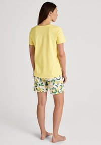 Gelbes Baumwoll-T-Shirt kombiniert mit cremefarbenen Shorts mit einem Zitronen- und Blattmuster. Das Outfit hat eine lässige Passform und ein einfaches Design.