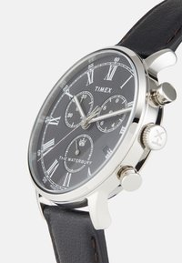 Montre chronographe avec un cadran noir, des aiguilles en acier argenté, des chiffres romains, un boîtier en acier inoxydable et un bracelet en cuir noir. Inclut des fonctions de minuteur.