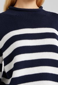 Marineblau-weiß gestreifter Strickpullover mit hohem Kragen, der ein strukturiertes Muster und einen lockeren Schnitt aufweist.