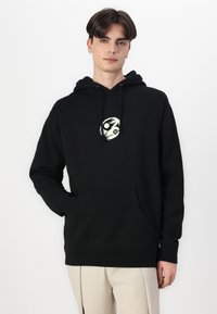 Μαύρη φούτερ μείγματος βαμβακιού, με κεντρικό γραφικό, ρυθμιζόμενα κορδόνια και μπροστινή τσέπη. Μαλακή υφή και χαλαρός σχεδιασμός.