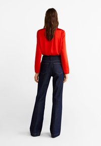 Blusa roja de manga larga combinada con jeans acampanados de cintura alta en azul oscuro. Los jeans tienen dos bolsillos traseros y un dobladillo limpio.