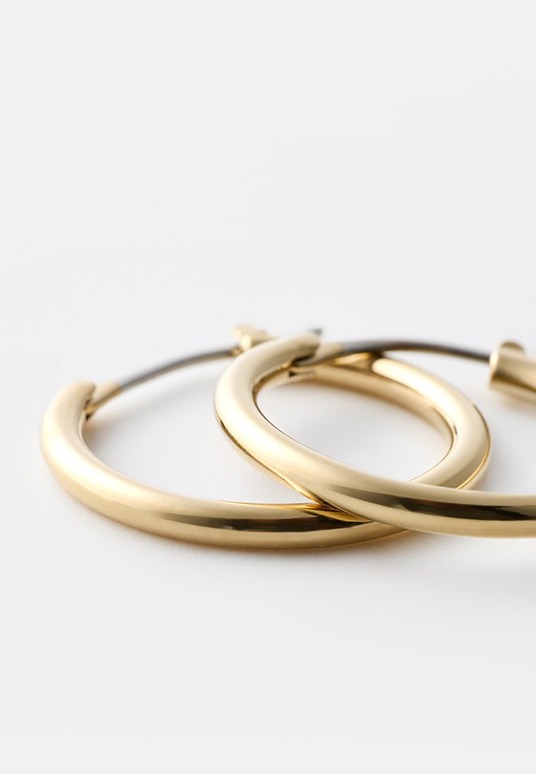Goldene Creolen mit einer glatten, polierten Oberfläche. Rundform, mittlere Größe, mit einem sicheren Verschluss. Einfaches und modernes Design.