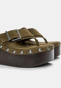 Brown suede platform sandals with a buckle strap and silver stud accents. Thick wooden sole with a curved shape, promoting ergonomic design.