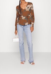 Blusa floreale marrone con scollo a V, maniche lunghe; abbinata a jeans svasati blu chiaro e sandali bianchi con cinturini. Porta una piccola borsa trapuntata.