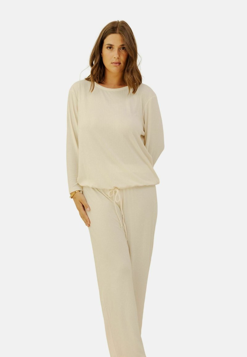 Ensemble de vêtements de détente beige clair en tissu texturé, comprenant un haut ample à manches longues et un pantalon à cordon de serrage avec une coupe décontractée.