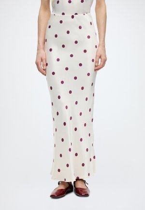 Weißer seidiger Maxirock mit verstreuten dunkelroten Punkten, getragen mit dunkelroten Mary-Jane-Schuhen.