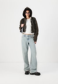 Cropped dark hooded jacket with toggle closures, white fitted top, light blue wide-leg jeans, and chunky black platform shoes.