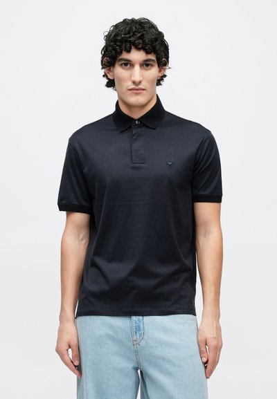 Tumši zils polo krekls no mīksta kokvilnas materiāla ar pogām aizdares apkakli, īsām piedurknēm un smalku logo krūšu zonā. Ikdienišķs piegriezums.