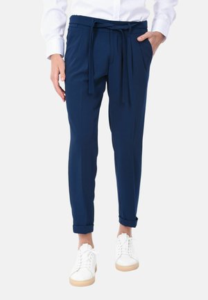 Pantaloni blu navy con vita regolabile, vestibilità affusolata, orli arrotolati e tasche laterali, abbinati a sneaker bianche. Tessuto dalla trama liscia.