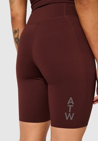 Burgundy atletiska shorts gjorda av elastiskt tyg med en mjuk textur. Har en hög midja och en grå "ATW"-logotyp på sidan.