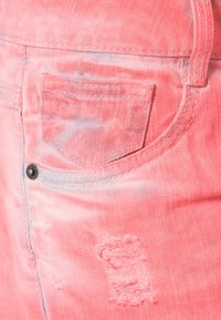 Ljust rosa denimtyg med en bakficka som har slitna detaljer och en metallknapp. Texturen är mjuk med en svag glans.