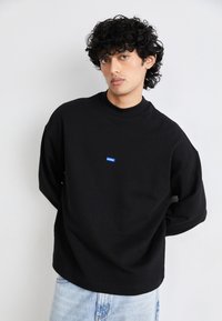 Zwarte sweatshirt met een hoge kraag en een relaxte pasvorm, voorzien van een klein blauw "HUGO" logo op de voorkant. Gemaakt van zachte, gestructureerde stof.