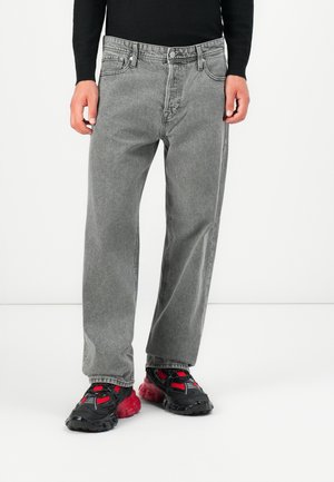 Gray denim jeans with a relaxed fit, five-pocket design, and visible stitching. Paired with black and red athletic shoes with textured detailing.