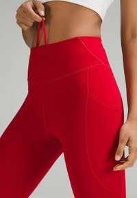 Leggings roșii cu talie înaltă din material elastic, dotate cu buzunare laterale și umplutură din plasă, având o textură netedă și un design ajustat.