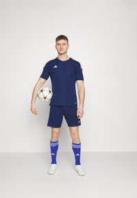 Jersey atlético de la marina y pantalones cortos con rayas blancas de Adidas, calcetines azules con rayas blancas, sosteniendo un balón de fútbol multicolor.