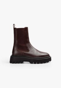 Botín de cuero marrón con suela de goma negra gruesa, paneles laterales elásticos y un tirador en el talón para facilitar su uso.