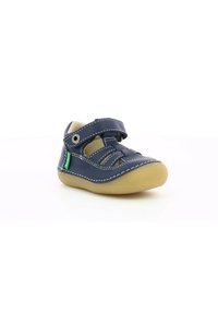 Zapato de cuero azul marino con dos correas de velcro ajustables, costuras beige, punta redondeada y una suela flexible de goma beige.