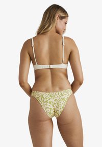 Bikini set s bledým topem s nastavitelnými ramínky a vzorovanými kalhotkami v tlumené zelené a béžové barvě, které zobrazují abstraktní organické tvary.