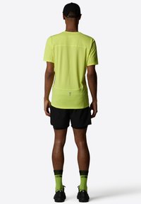 Kortärmad neon gul träningströja kombinerad med svarta shorts och neongröna strumpor. Har reflexdetaljer och en lätt design.