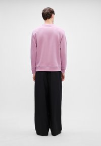 Sudadera de color púrpura claro con puños y dobladillo acanalados, combinada con pantalones negros holgados. La vista desde atrás muestra un diseño minimalista y un acabado sin costuras.