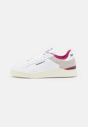 White sneaker featuring a leather and suede upper, pink lining, and a multi-colored accent on the heel. Flat laces and a rubber sole.