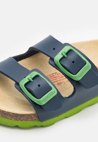 Blå lädersandal med gröna spännen, korkfotbädd och strukturerad grön sula. Märket "superfit" ingraverat på spännena.