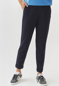 Pantaloni tapered blu realizzati in tessuto a trama con tasche laterali, orlo a risvolto e abbinati a sneaker grigie e bianche.