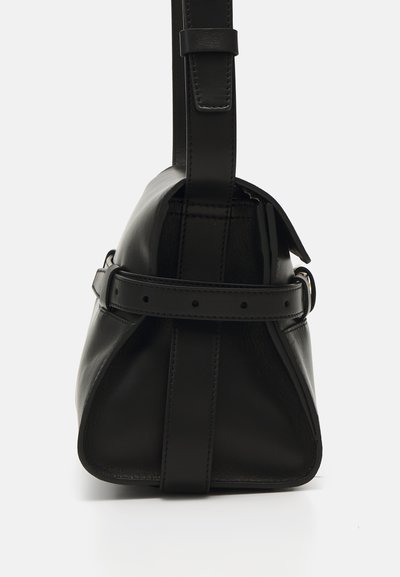 Bolsa de mão em pele preta com um formato triangular, apresentando uma alça longa e ajustável e uma aba frontal presa por uma tira com furos para ajustes.