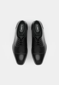 Zapatos de vestir de cuero negro con un acabado suave, punta redondeada y diseño con cordones. Presentan costuras sutiles y un logo en las plantillas.