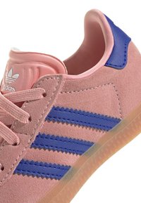 Baskets en daim rose avec des rayures bleues et des accents en cuir. Elles présentent des lacets ronds et une semelle en caoutchouc texturée. Marquage sur la languette.