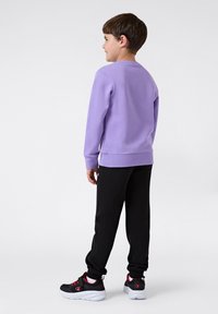 Lila sweatshirt gemaakt van zachte stof met lange mouwen, gecombineerd met zwarte joggingbroeken en zwarte sneakers met rode accenten.