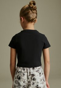Musta lyhythihainen crop-top t-paita, jossa on pyöreä kaula-aukko, yhdistettynä kukkakuosisin housuihin, joissa on taskut.