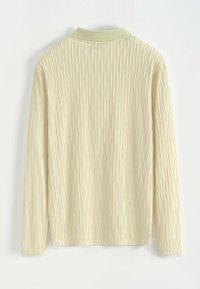 Haut à manches longues jaune pâle avec un motif texturé de lignes verticales, doté d'un col à revers et de poignets légèrement élastiqués.