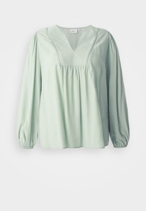 Svetlo zelena bluza z dolgimi rokavi in V-izrezu, z nabranim bodicem in dekorativnim šivanjem ob izrezu. Mehka tekstura, sproščen kroj.