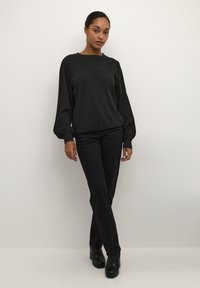 Pull noir à manches longues côtelé avec des manches bouffantes, associé à un jean noir ajusté et des bottes à talons noires, sur un fond neutre.