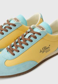 Chaussures de jogging en suède jaune et bleu clair avec tissu, lacets marron et logo "le Fleur Jogger" sur le côté.