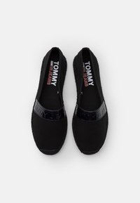 Zwarte instapschoenen met een stoffen bovenwerk, glanzende zwarte logoband en gevlochten zooldetails. Voorzien van een gevoerde binnenzool voor comfort.