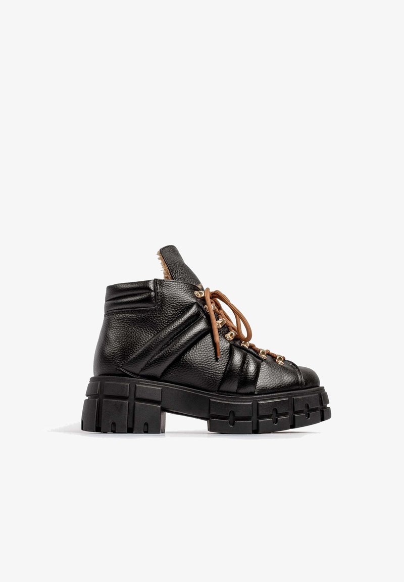 Botte noire en cuir montant à la cheville avec une semelle épaisse à crampons, lacets marron, design rembourré et œillets en métal, vue de côté extérieur sur fond blanc.