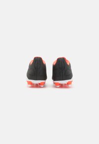 Scarpe da calcio nere con accenti rossi, design elegante, superficie testurizzata e suola bianca dotata di più tacchetti per una migliore aderenza.