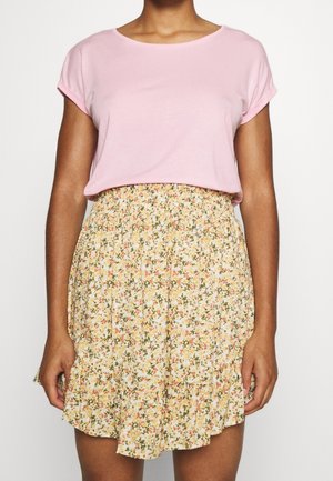 Rosa Baumwoll-T-Shirt kombiniert mit einem gelben Blumendruck-Rock, der einen gerafften Bund und einen Rüschensaum aufweist. Das Blumenmuster enthält grüne und orangefarbene Akzente.